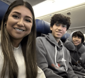 Three friends on an airplane taking a selfie, smiling at the camera from their seats in a cabin.